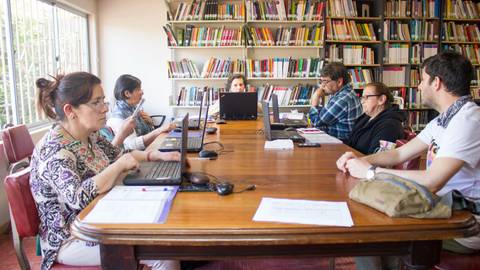 Un grupo de personas trabaja en un aula frente a computadoras mientras están rodeados de estanterías llenas de libros.