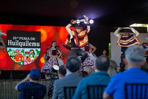 Un grupo de bailarines en un escenario durante la 25ª Feria de Huilquilemu, mostrando trajes tradicionales y una animada actuación.