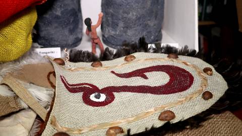 La imagen muestra un objeto decorativo con un diseño en forma de serpiente, junto a figuras en un entorno que sugiere un contexto cultural.