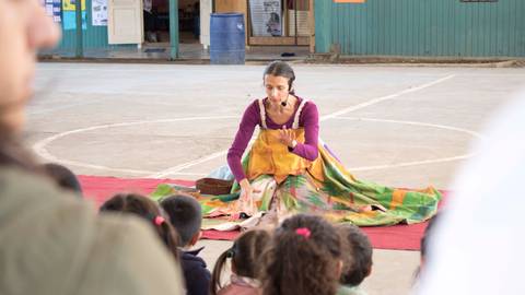 Una cuentacuentos atrapa la atención de un grupo de niños en un espacio al aire libre.