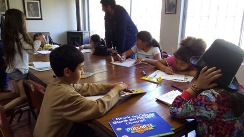Un grupo de niños y adultos está trabajando en un taller de arte en una sala iluminada.
