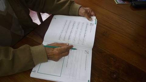 Una persona mayor está escribiendo en un cuaderno sobre una mesa de madera.