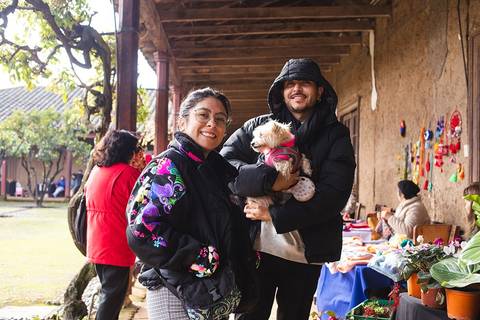 Una pareja sonriente sostiene a un perro en un mercado al aire libre.