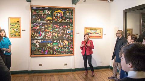 Una guía explica una obra de arte en una galería con varias personas observando.