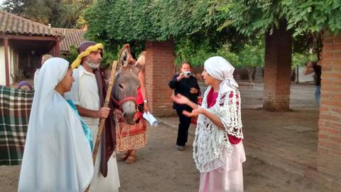 Un grupo de personas vestidas con trajes tradicionales interactúan junto a un burro en un entorno rural.
