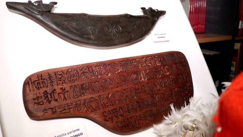 La imagen muestra dos objetos arqueológicos, uno oscuro en la parte superior y otro de color marrón con inscripciones en la parte inferior.