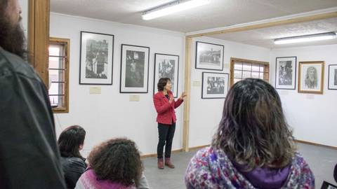 Una mujer está dando una charla en una galería de arte con fotografías en las paredes.