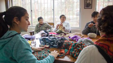 Un grupo de mujeres se reúne para tejer en una mesa, compartiendo momentos y habilidades en un ambiente camaraderil.