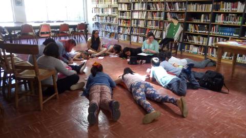 Un grupo de personas se encuentra acostado en el suelo de una biblioteca mientras realizan una actividad en grupo.