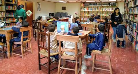 Un grupo de niños está leyendo en una biblioteca con estanterías llenas de libros.