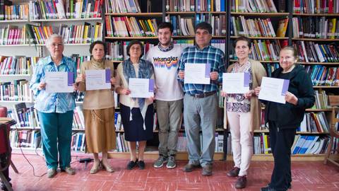 Grupo de personas sosteniendo certificados en una biblioteca.