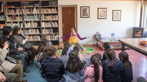 Una narradora está contando una historia a un grupo de niños en un salón con estanterías de libros.