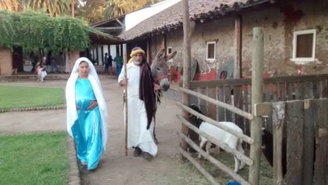 Una mujer y un hombre vestidos con ropas tradicionales caminan junto a un burro en un entorno rural.