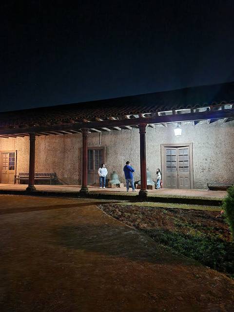 Una escena nocturna en un edificio con arquitectura antigua, donde varias personas conversan bajo la luz de un foco.