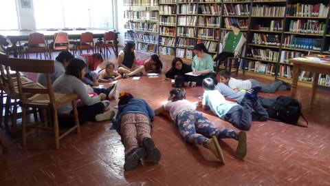 Un grupo de jóvenes está en el suelo de una biblioteca, trabajando en actividades grupales.