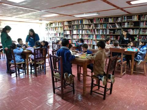 Un grupo de niños y adultos trabajando en mesas dentro de una biblioteca.