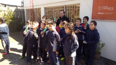 Un grupo de niños y un adulto posan frente a un edificio con una señalización de la Universidad Católica.