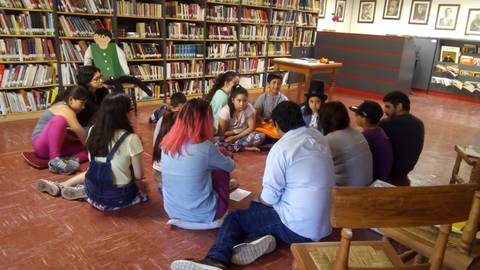 Un grupo de jóvenes se reúne en círculo en una biblioteca para participar en una actividad de grupo.