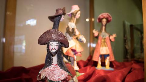 Una colección de figuras artesanales monumentales con vestimentas coloridas exhibidas en un estante.