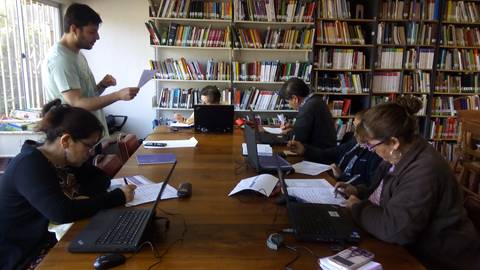 Un grupo de personas trabajando en una biblioteca, con un hombre de pie presentando un documento.