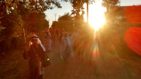 Una procesión de personas camina por un camino al atardecer, con el sol brillando detrás de ellos.