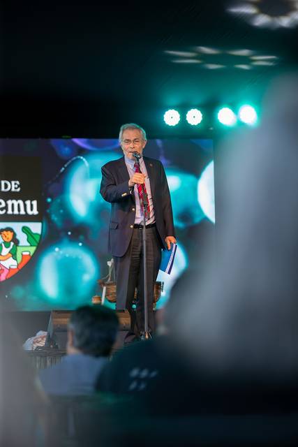 Un hombre de pie con un micrófono habla ante un público en un evento.