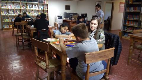 Un grupo de niños y jóvenes trabaja en una actividad en una biblioteca con mesas y estanterías llenas de libros.