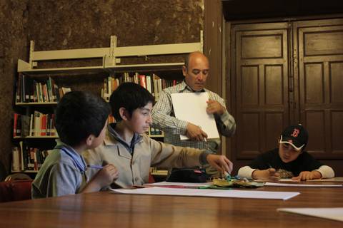 Un grupo de niños y un adulto están en una sala de clase con materiales de dibujo.