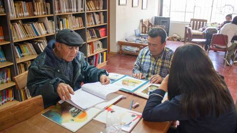 Un grupo de personas estudian y conversan en una biblioteca.