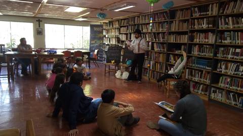 Una reunión en una biblioteca donde un narrador cuenta historias a niños sentados en el suelo.