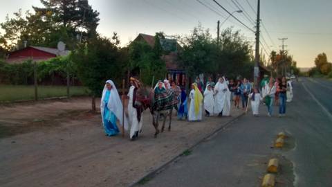 Un grupo de personas vestidos con túnicas caminan por una calle rural durante un atardecer.