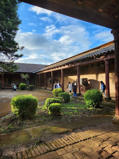 Una construcción tradicional rodeada de plantas y un cielo parcialmente nublado.