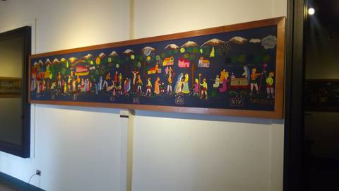 Una colorida pintura mural que representa diversas escenas de la vida cotidiana en un entorno rural con montañas al fondo.