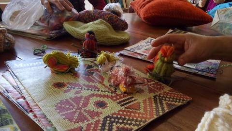 La imagen muestra un grupo de figuras hechas a mano con hilos sobre una mesa con revistas y materiales de costura.