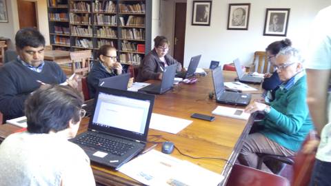 Un grupo de personas trabaja en laptops alrededor de una mesa en un entorno académico.