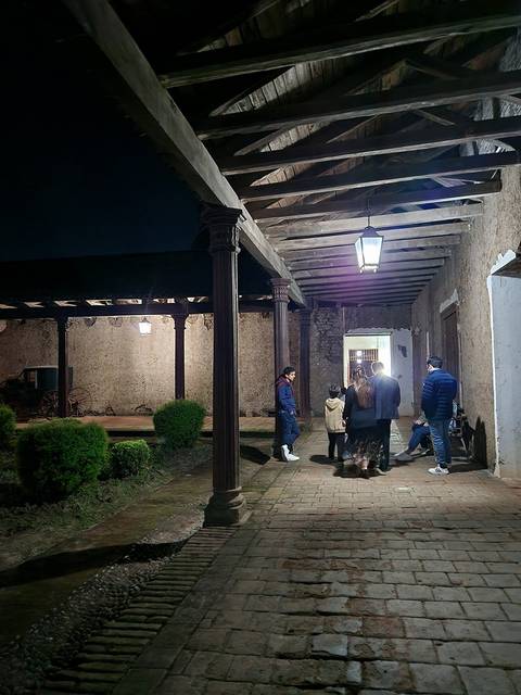 Un grupo de personas conversando en un pasillo iluminado por una lámpara en un entorno rústico.