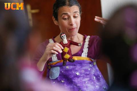 Una mujer sostiene una marioneta mientras cuenta una historia a un grupo de niños.