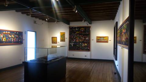 Una sala de exposición con pinturas en las paredes y una vitrina en el centro.