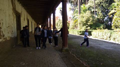 Un grupo de personas camina por un pasillo con columnas y una zona ajardinada al fondo.
