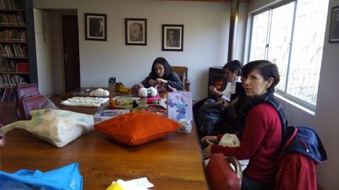 Un grupo de personas se reúne en una sala con una mesa de madera, realizando actividades manuales y conversando.