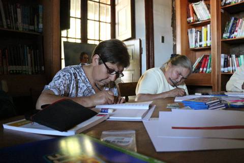 Dos personas mayores están escribiendo en una biblioteca.