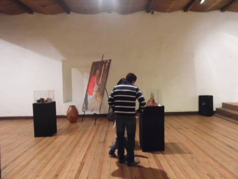 La imagen muestra a dos personas observando obras de arte en una galería con un piso de madera.