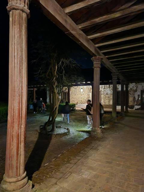 Una escena nocturna en un pasillo con columnas y un par de personas conversando en un ambiente tranquilo.