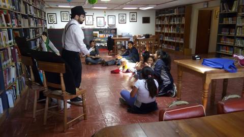 Un narrador cuenta historias a niños sentados en el suelo de una biblioteca.