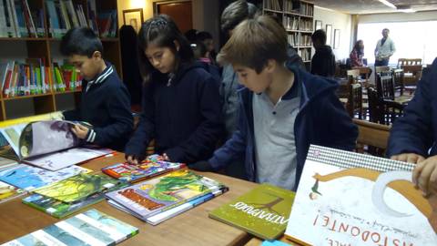Un grupo de niños está revisando libros en una biblioteca.