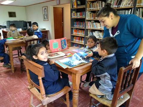 Un grupo de niños y una adulta interactúan en una biblioteca mientras revisan libros en una mesa.