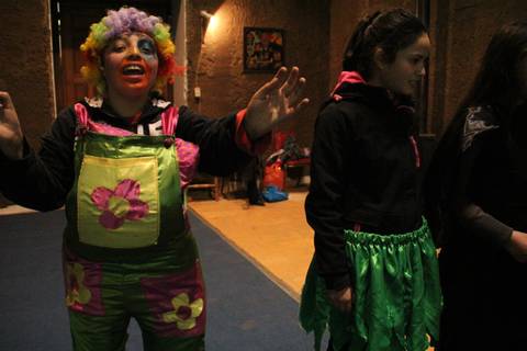 Una payasa con vestido colorido y una niña vestida de verde en un ambiente festivo.
