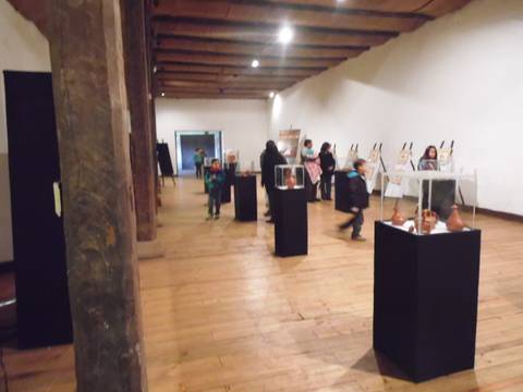 Una sala de exposiciones con varias personas observando obras en pedestales.