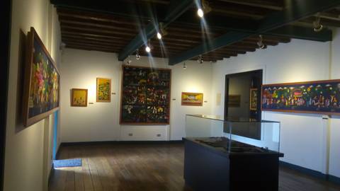 El interior de una galería de arte con varias obras en las paredes y una vitrina en el centro.