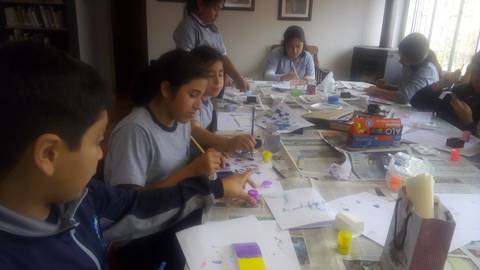 Un grupo de niños y niñas están pintando y creando manualidades en una mesa llena de materiales artísticos.